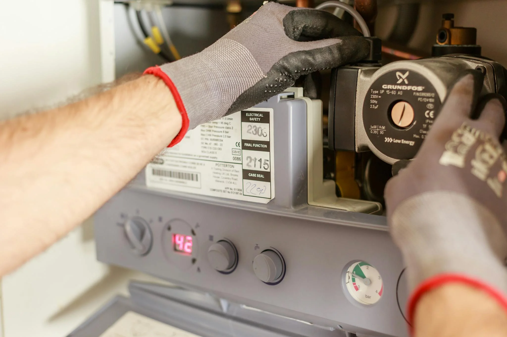 FlameTech technician servicing a boiler — circulator pump and pressure-gauge panel visible